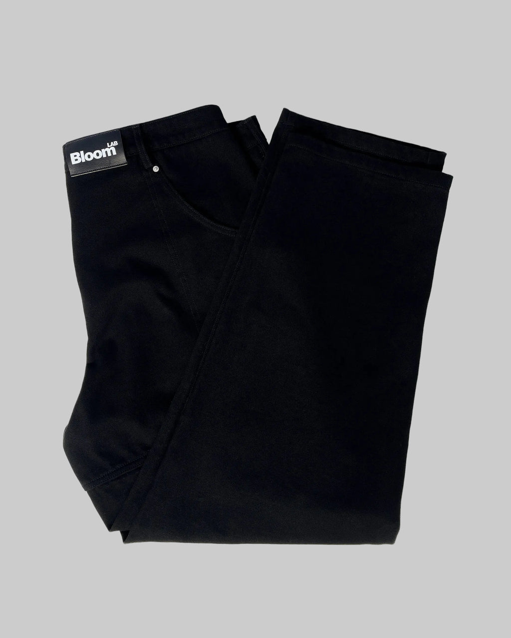 Folded black pants with a 'Bloom' label on a white background